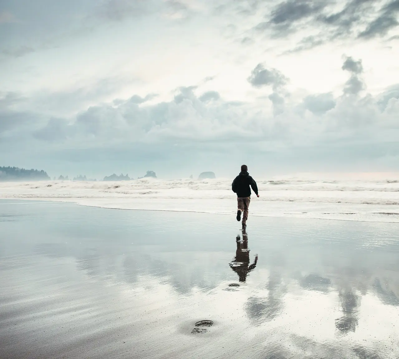 A runner on a reflective beach at dawn