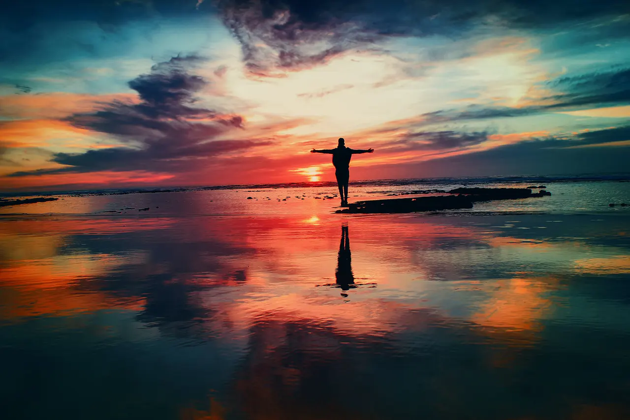 A person standing with arms wide open at sunrise by the water